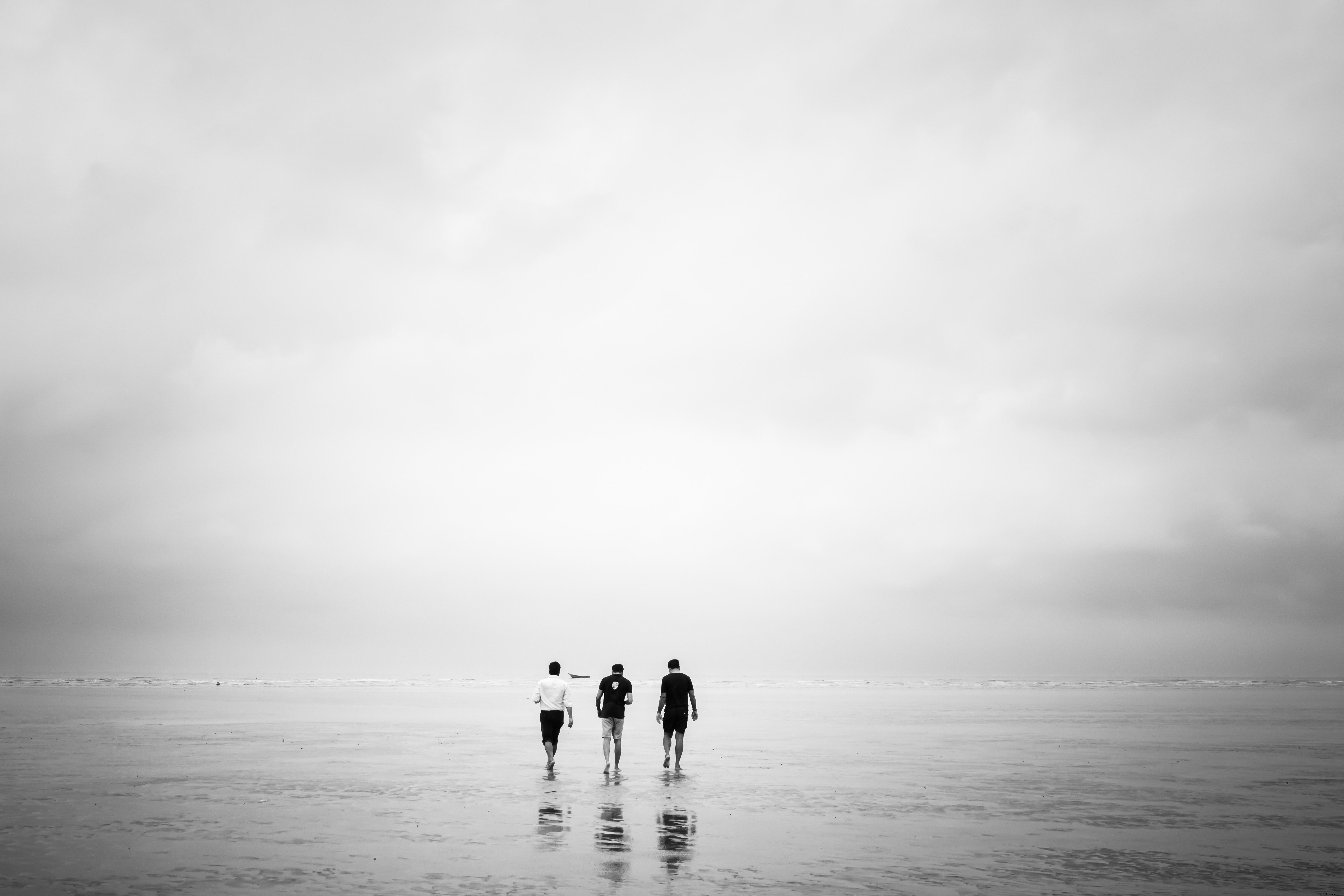 干潮時のビーチで写真の上を歩く3人の男性