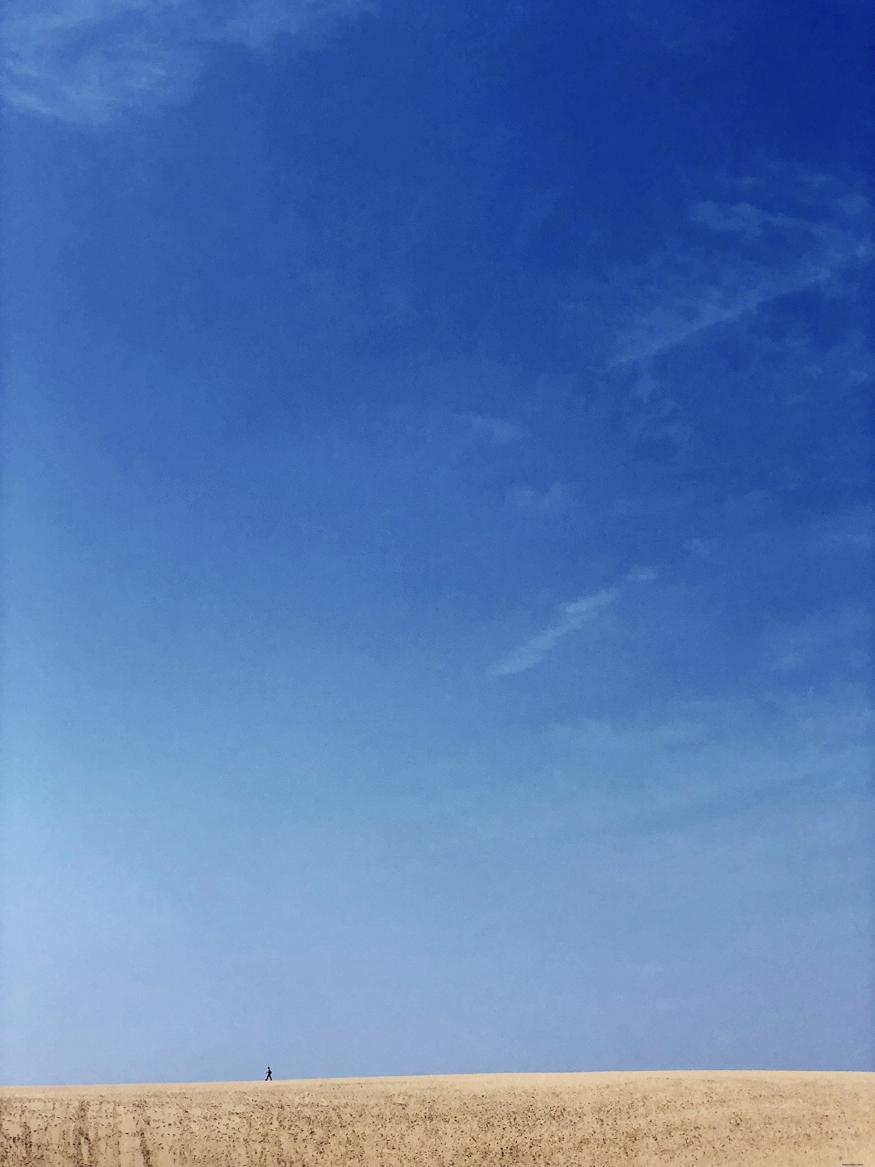 砂漠と空の境界を歩く孤独な人物の写真