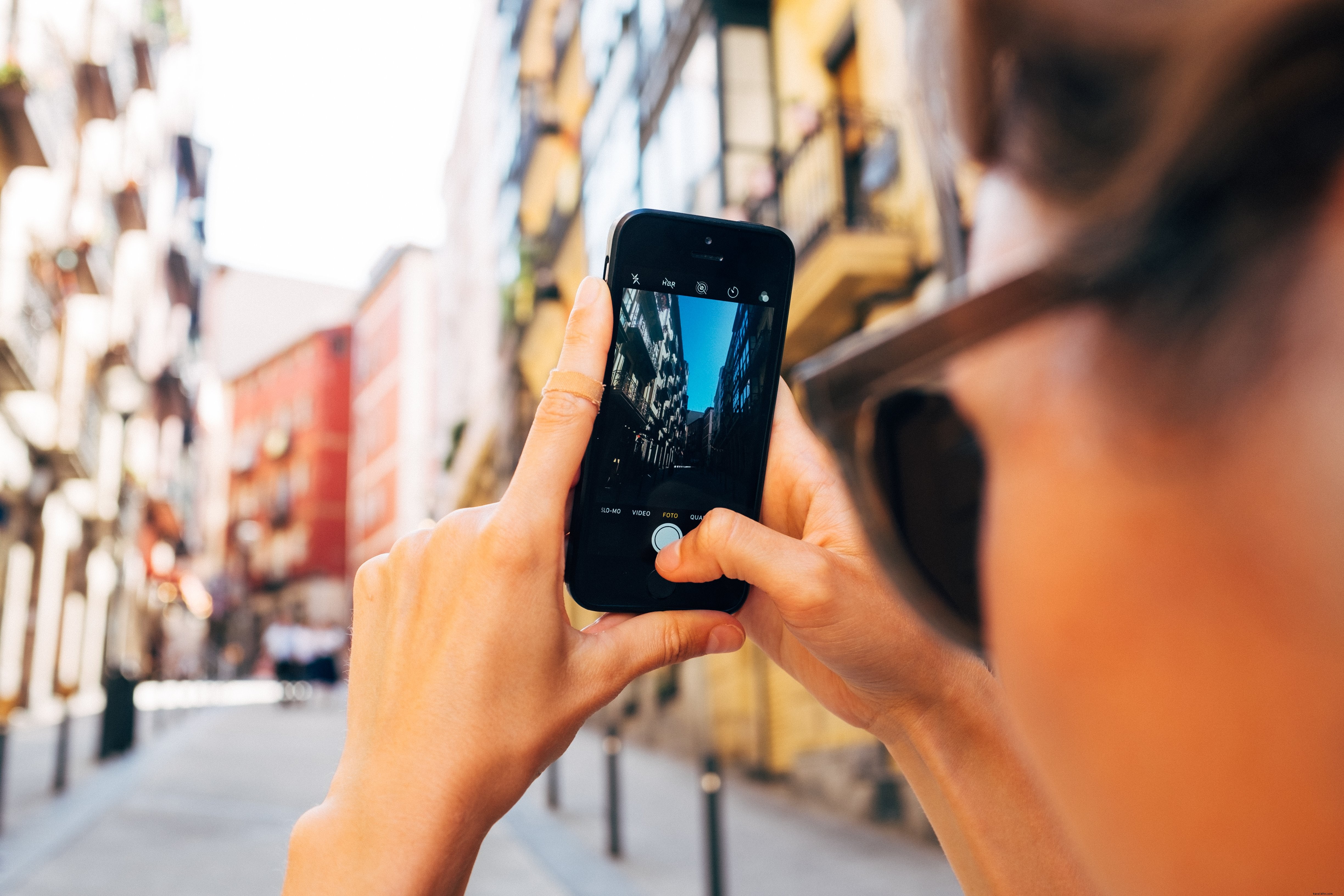 女性がスマートフォンで日差しの強い街角の写真を撮影
