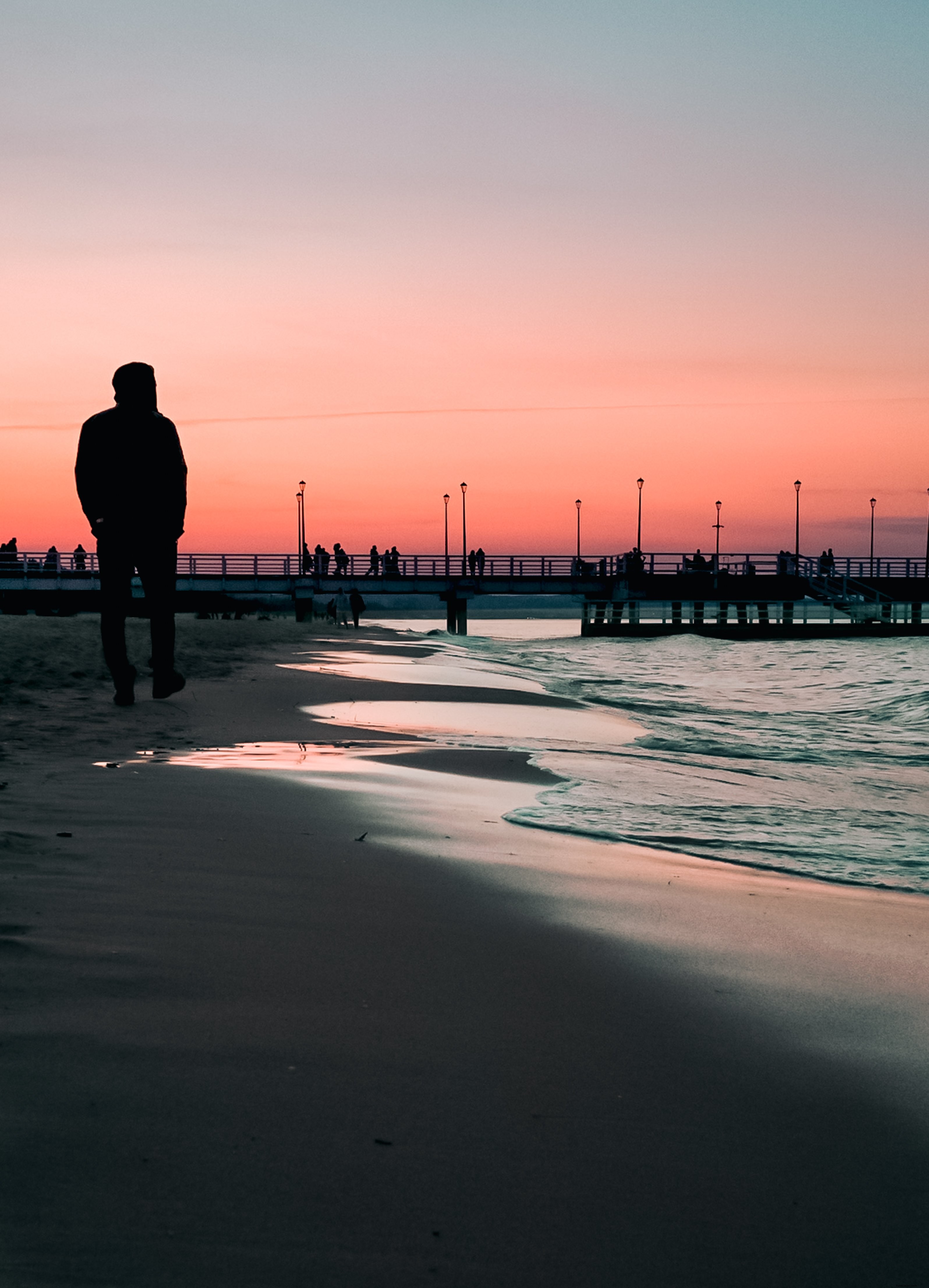遠くの桟橋と夕日が映えるビーチウォークの写真