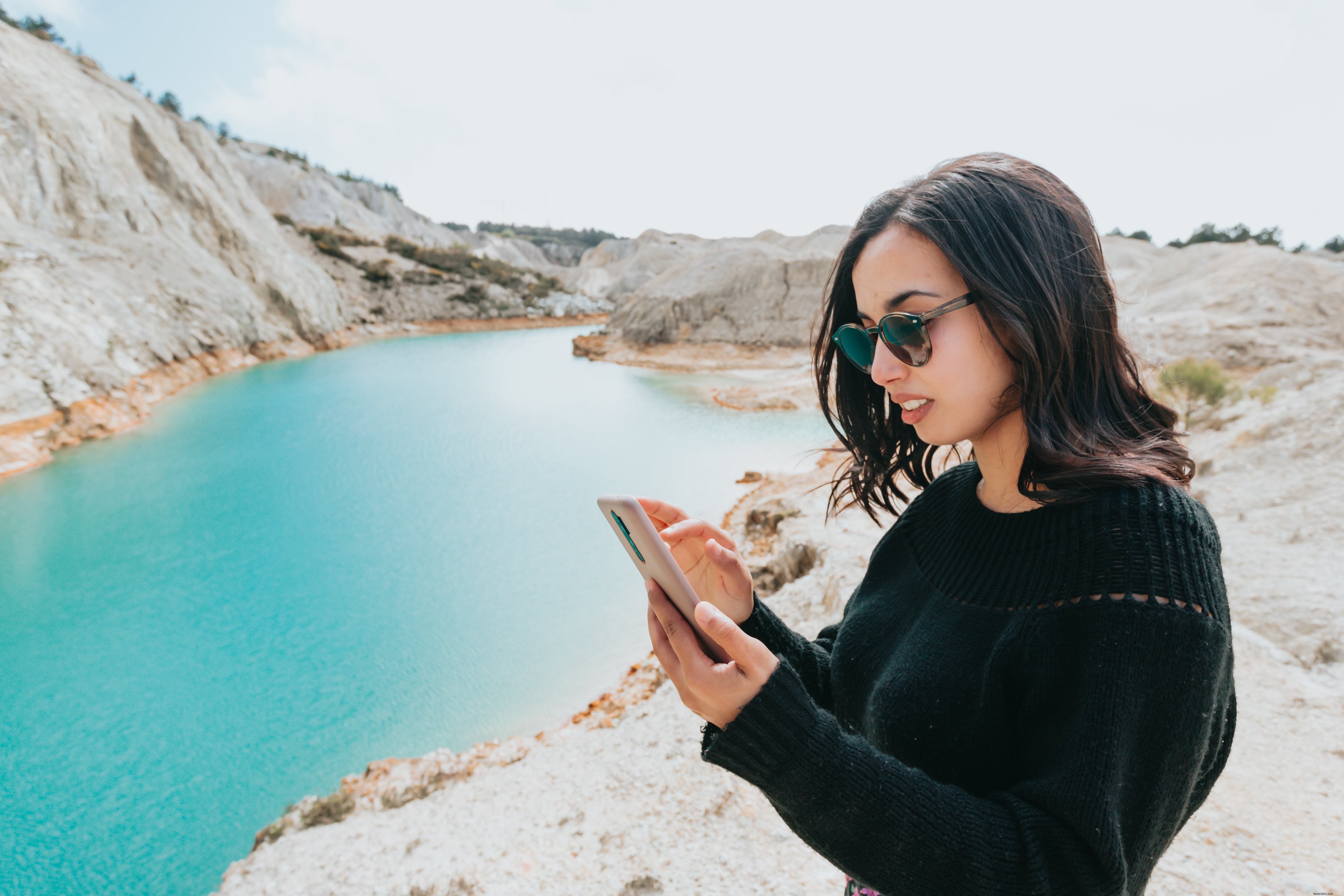 青い水辺でスマートフォンを見る女性